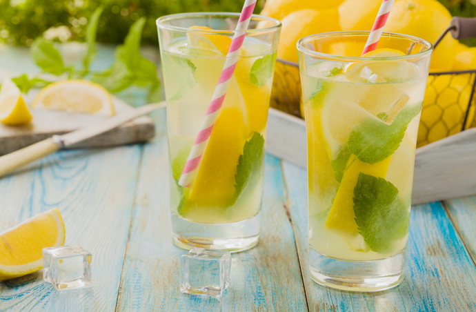 lemonade with mint and on rocks served in a glass with a straw on a wooden table.